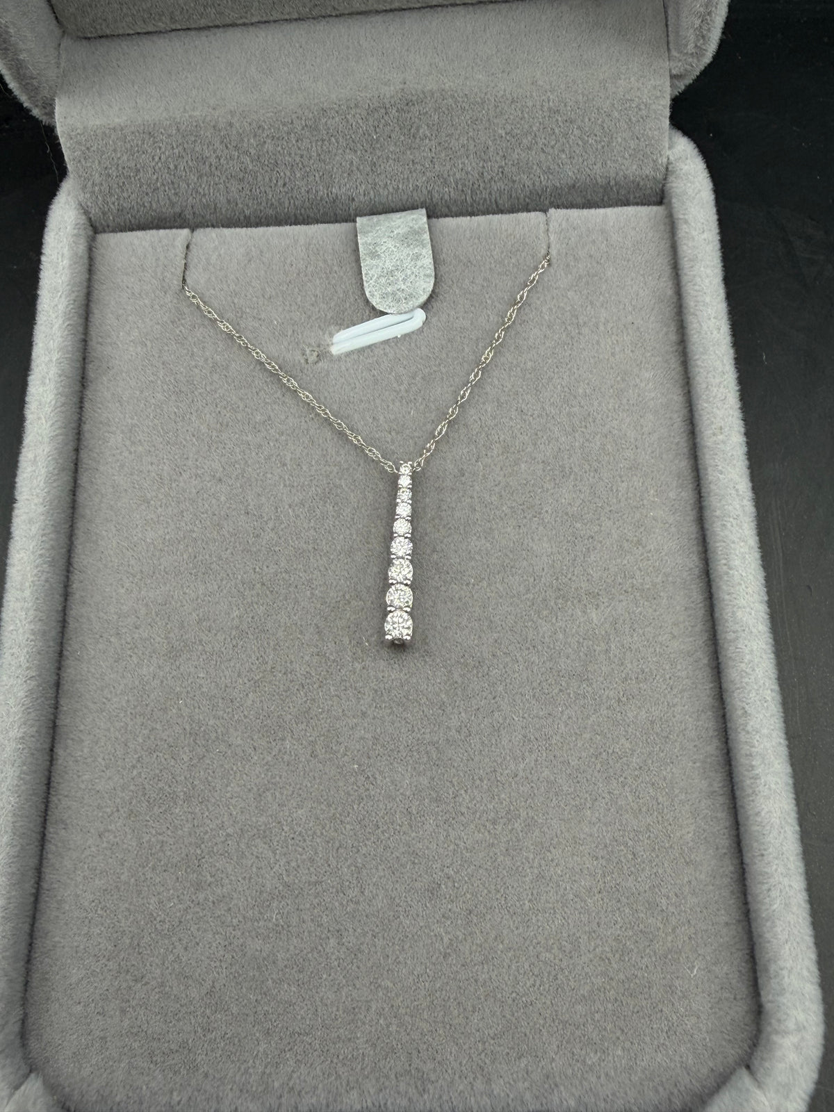 White gold necklace with a graduated natural diamond bar pendant displayed in a gray jewelry box